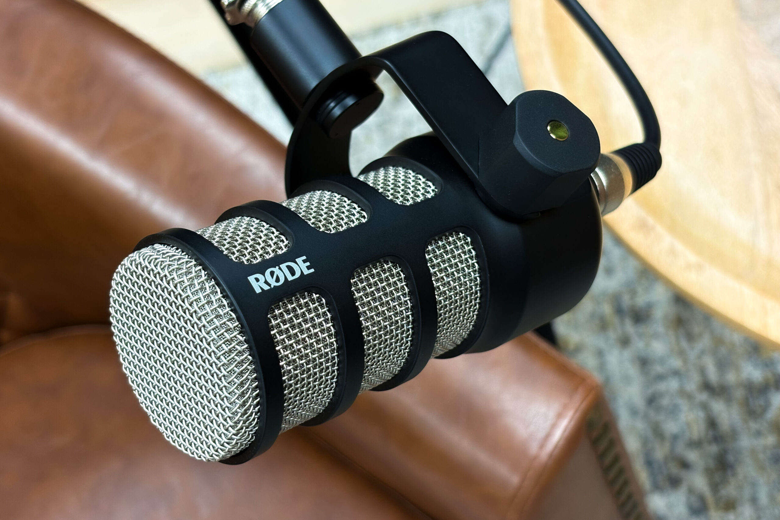 Close-up of a Rode microphone in a black shock mount, held near a brown surface.